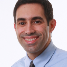 Portrait of Dr. Daniel Adolfo Llano, smiling at the camera in a light blue shirt and dark striped tie