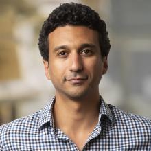 Portrait of Dr. Eiman Azim looking straight at the camera with a smirk wearing a gingham collared shirt.
