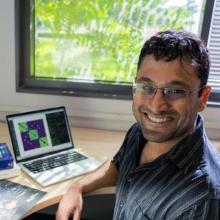Photo of Dr. Rishidev Chaudhuri smiling brightly while sitting at a computer in front a sunny window