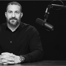 Portrait of Dr. Huberman in black and white siting in front of an audio microphone