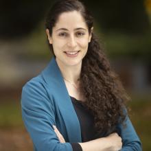 Portrait of Dr. Leenoy Meshulam, smiling with arms crossed looking straight at the camera in a blue sweater